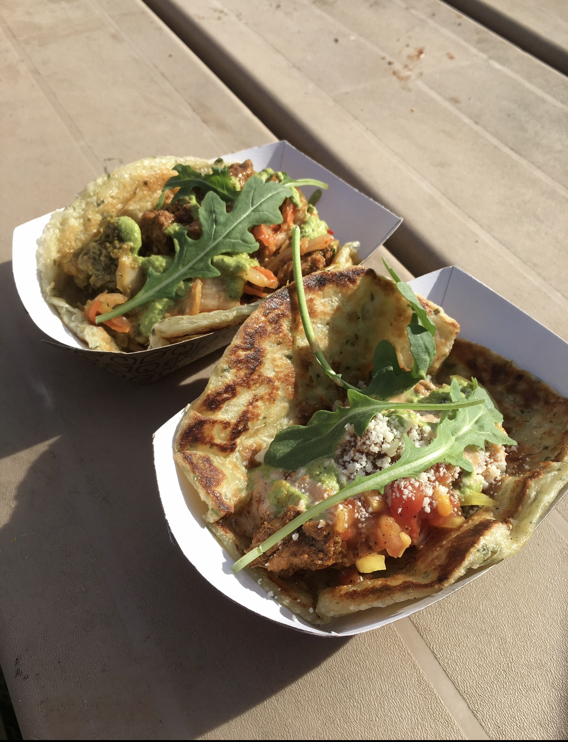 Two roti rolls filled and topped with arugula, served in paper boats
